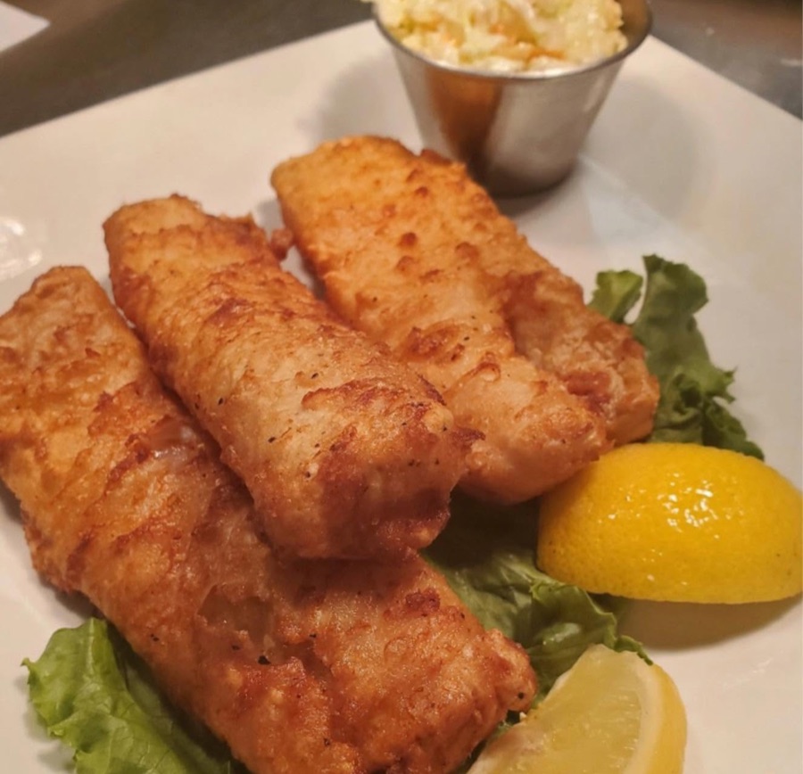 Beer-battered cod fillets on lettuce with lemon wedges and coleslaw
